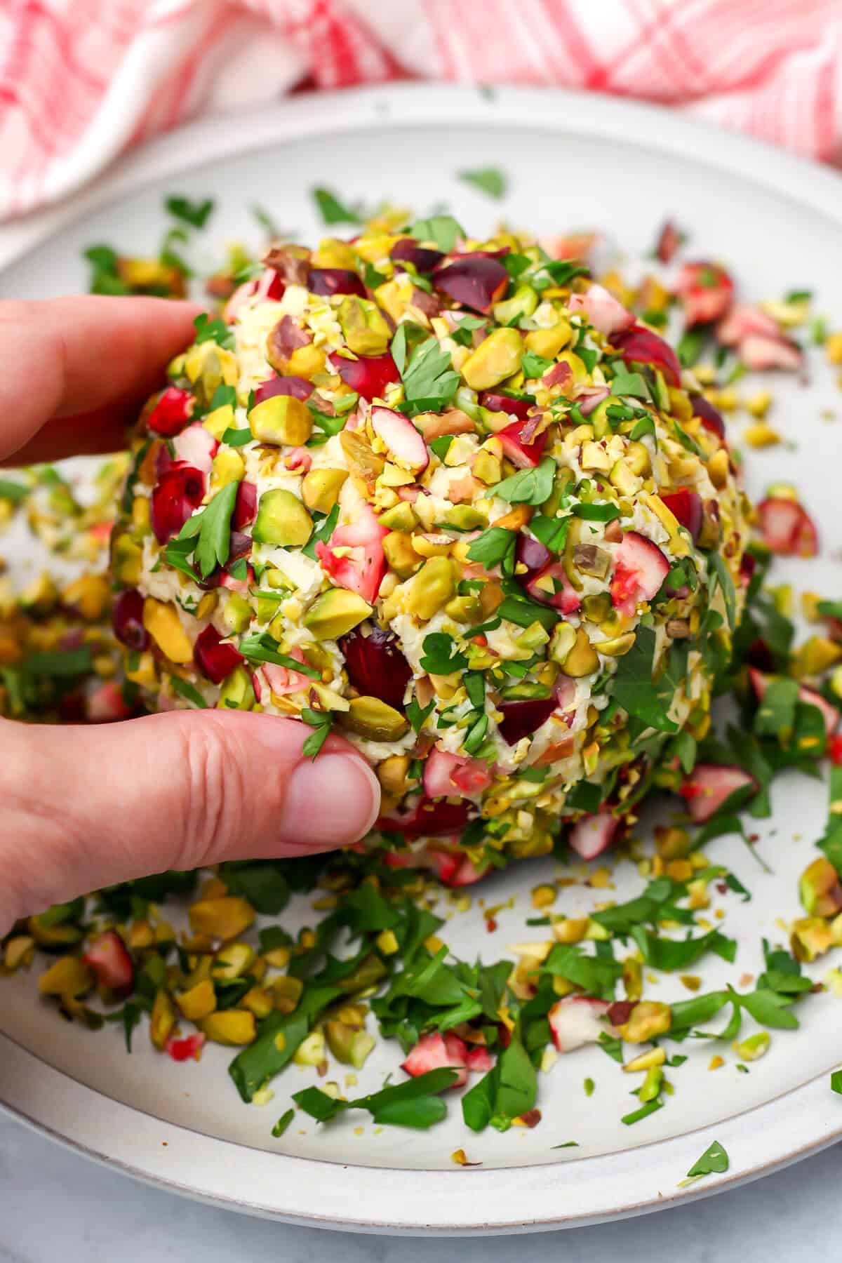 Rolling a vegan cheese ball made from tofu in chopped nuts, herbs, and cranberries.