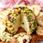 A vegan cheese ball made with tofu and herbs on a cutting board surrounded with cracker.