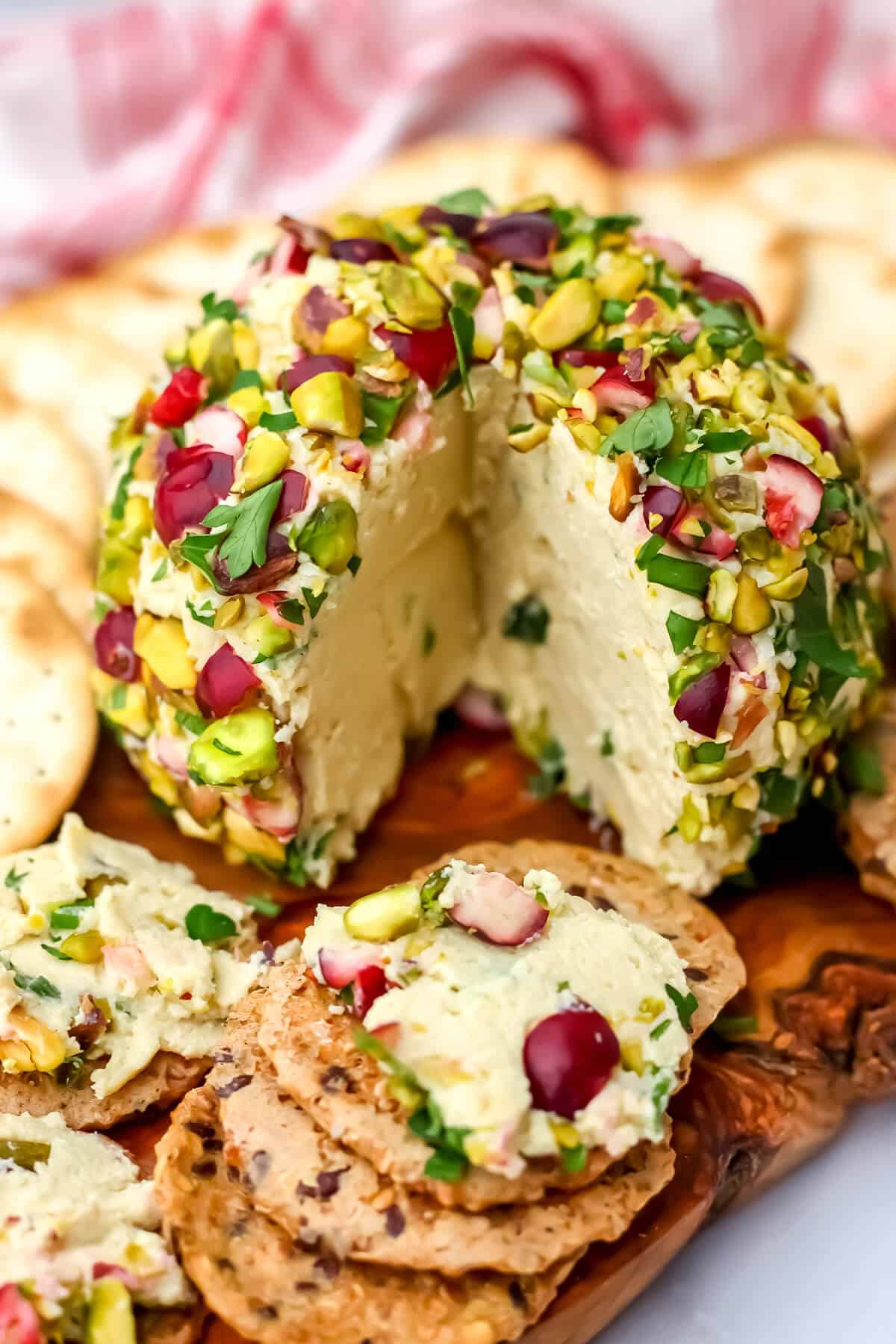 A vegan cheese ball on a cutting board with a slice taken out of it and spread on a cracker.