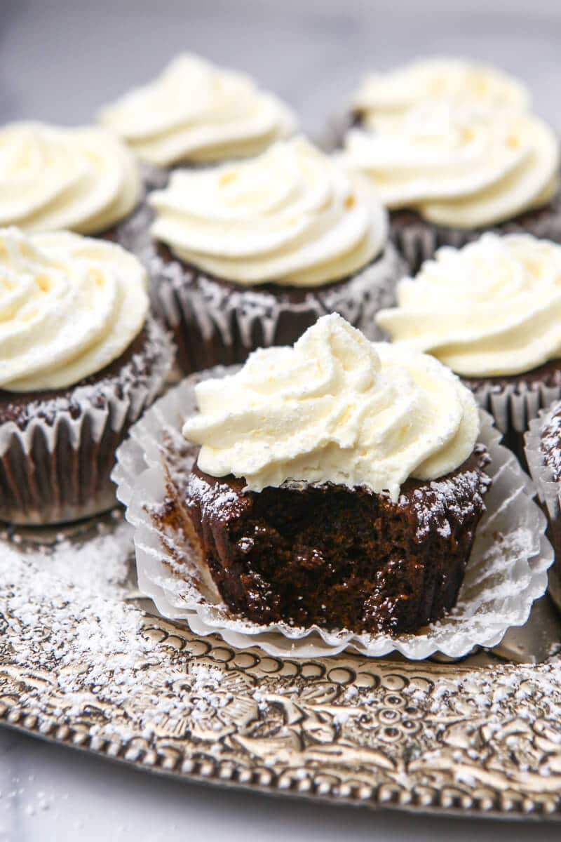 Vegan gingerbread cupcakes with lemon frosting sprinkled with powdered sugar on a sliver tray.