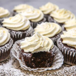 Vegan gingerbread cupcakes with lemon frosting on a decorative serving plate with powdered sugar sprinkled over them.