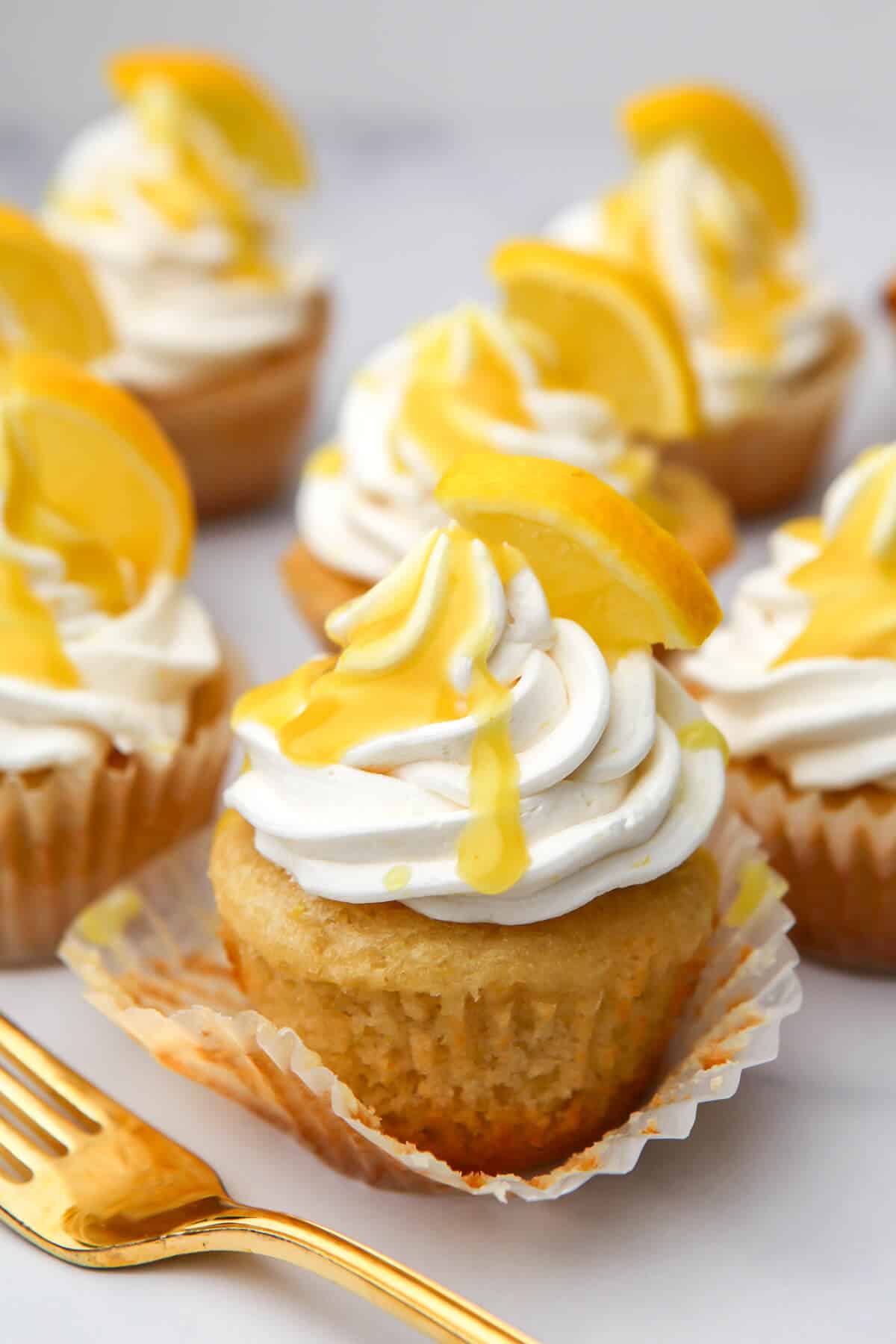 A bunch of lemon cupcakes with vegan lemon buttercream frosting on top and a for on the side.