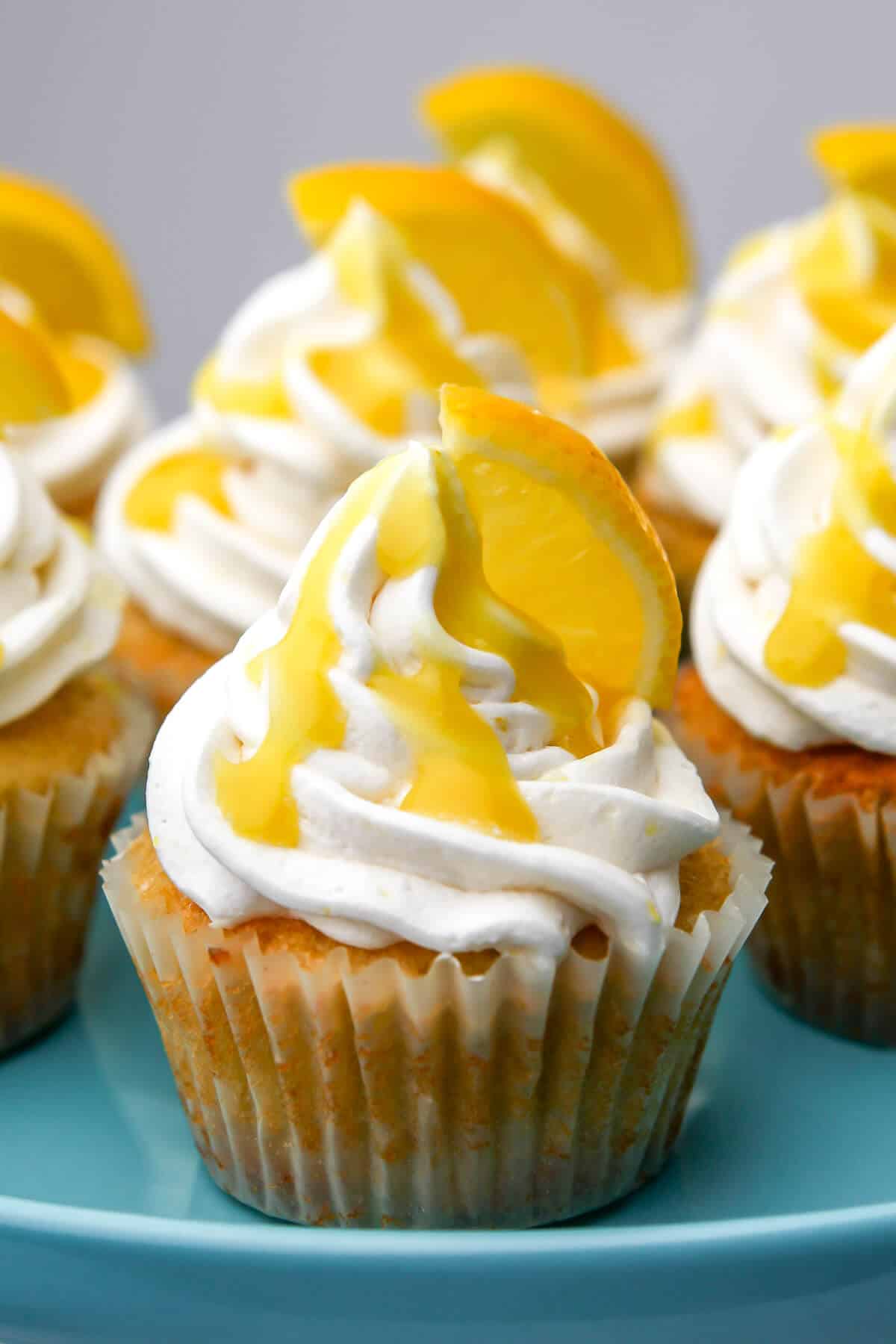 Vegan lemon frosting on cupcakes that are sitting on a blue cake dish.
