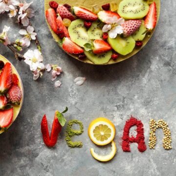 A bowl of fruit with the word vegan spelled out next to it in fruit.