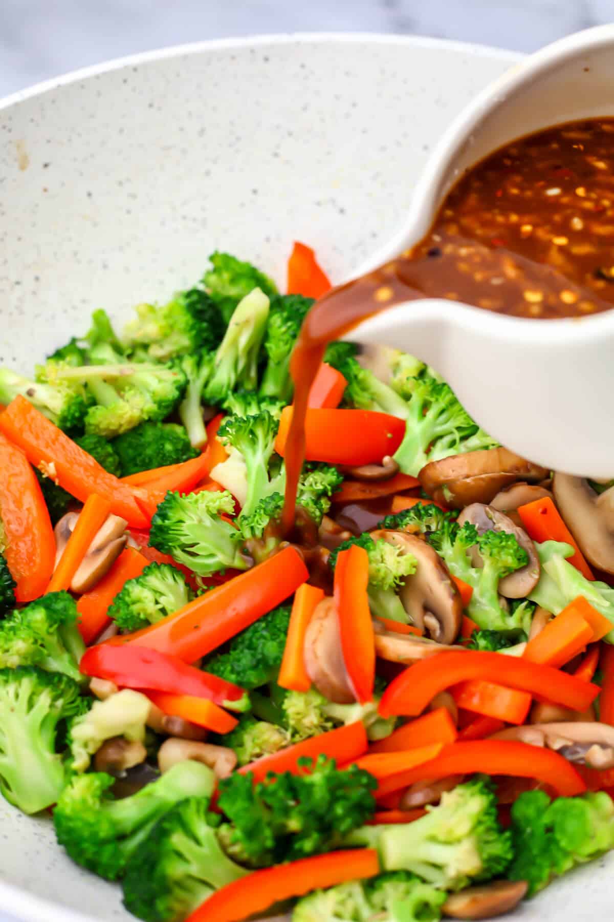 Stir-fry sauce being poured over stir-fried veggies in a wok.