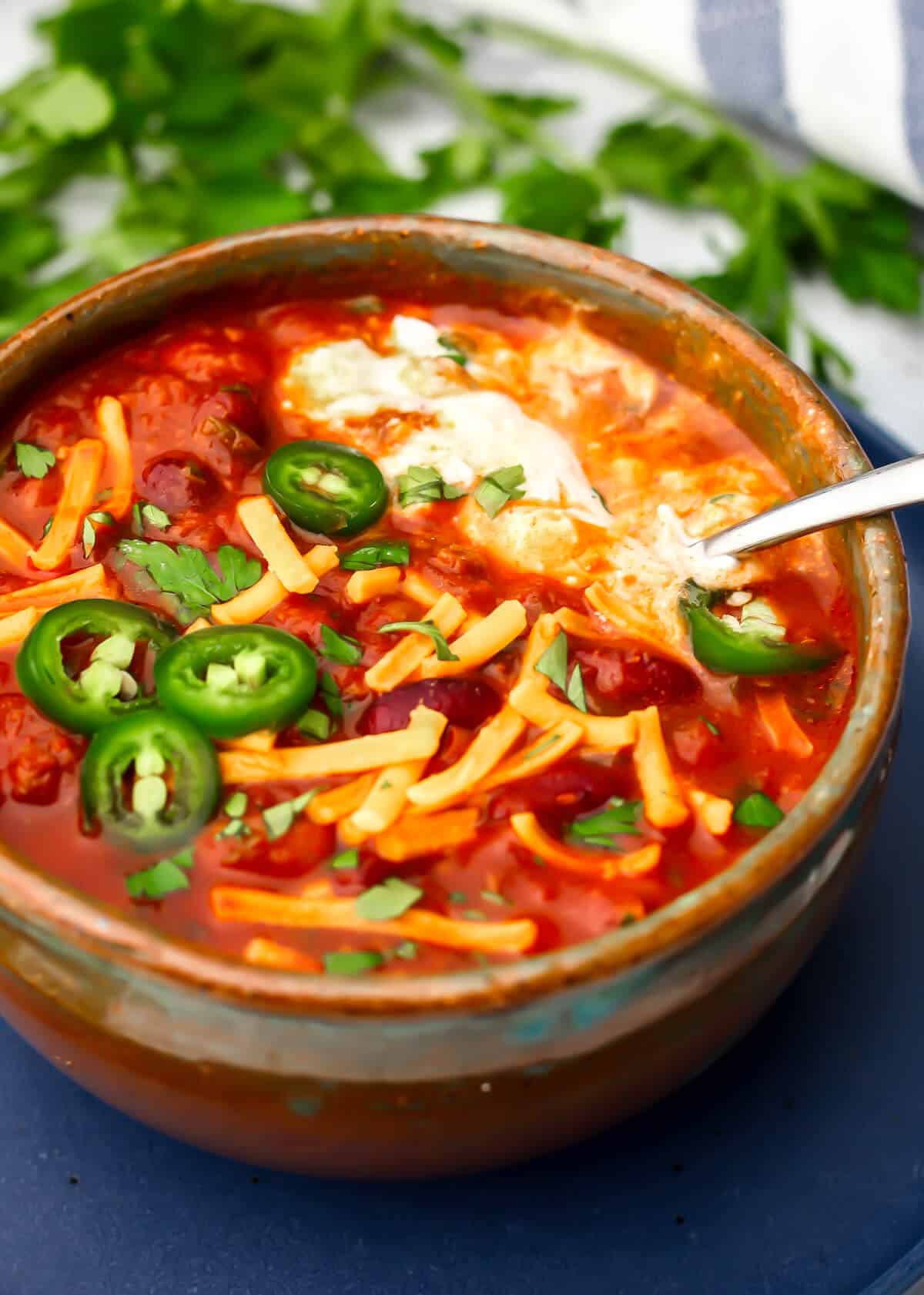 A bowl of Impossible chili with vegan cheese, vegan sour cream, and jalapenos on top.