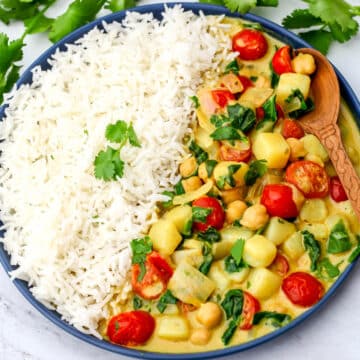 A plate full of chickpea potato spinach curry with white rice on one side and cilantro behind it.
