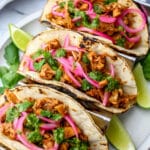Three vegan jackfruit tacos with Mexican pickled red onions and garlic cilantro sauce on top.