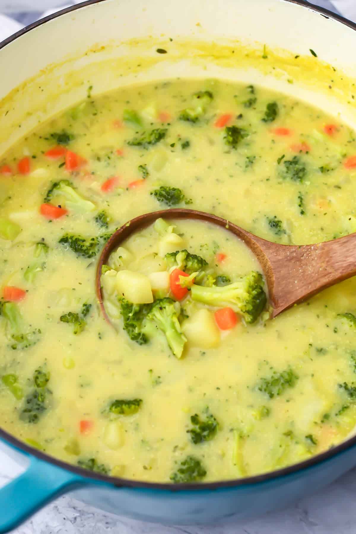 Vegan broccoli and potato soup in a large soup pot being scooped up with a wooden ladle.