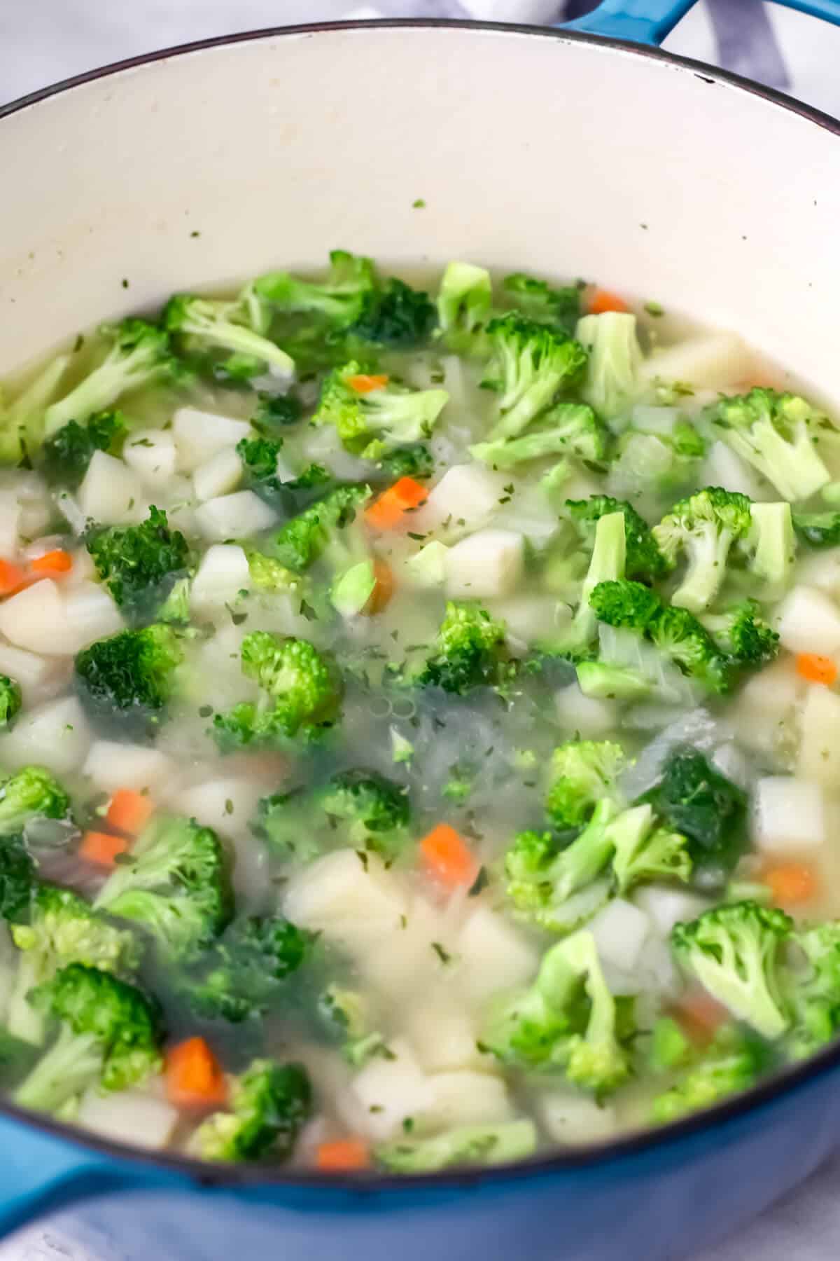 Potatoes, carrots, and broccoli in a soup pot cooking in broth.