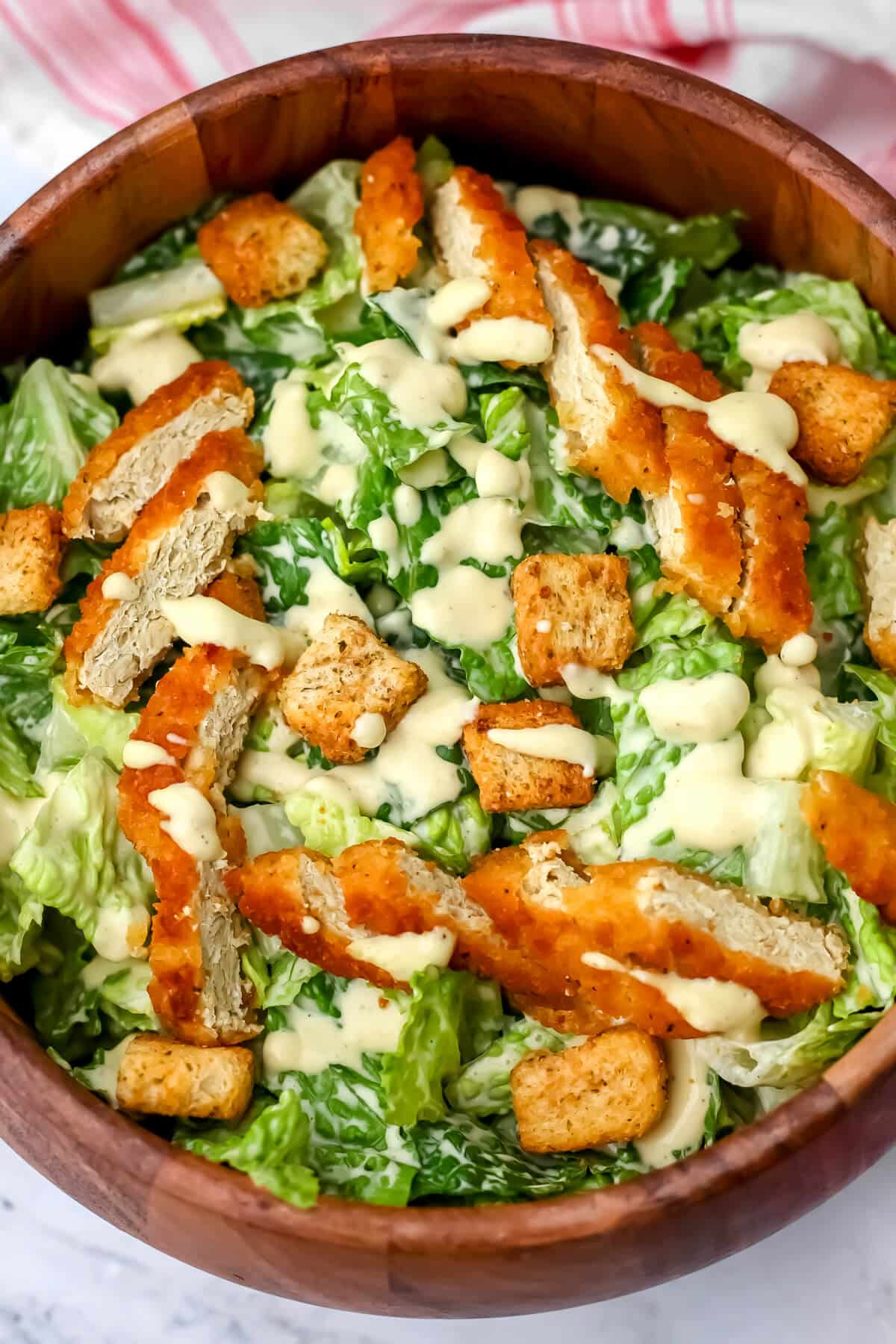 A top view of a wooden salad bowl filled with Romain lettuce with vegan Caesar dressing, vegan chicken, and croutons on it.