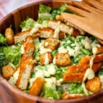 A vegan chicken Caesar salad with sliced vegan chicken strips and croutons on Romaine lettuce.