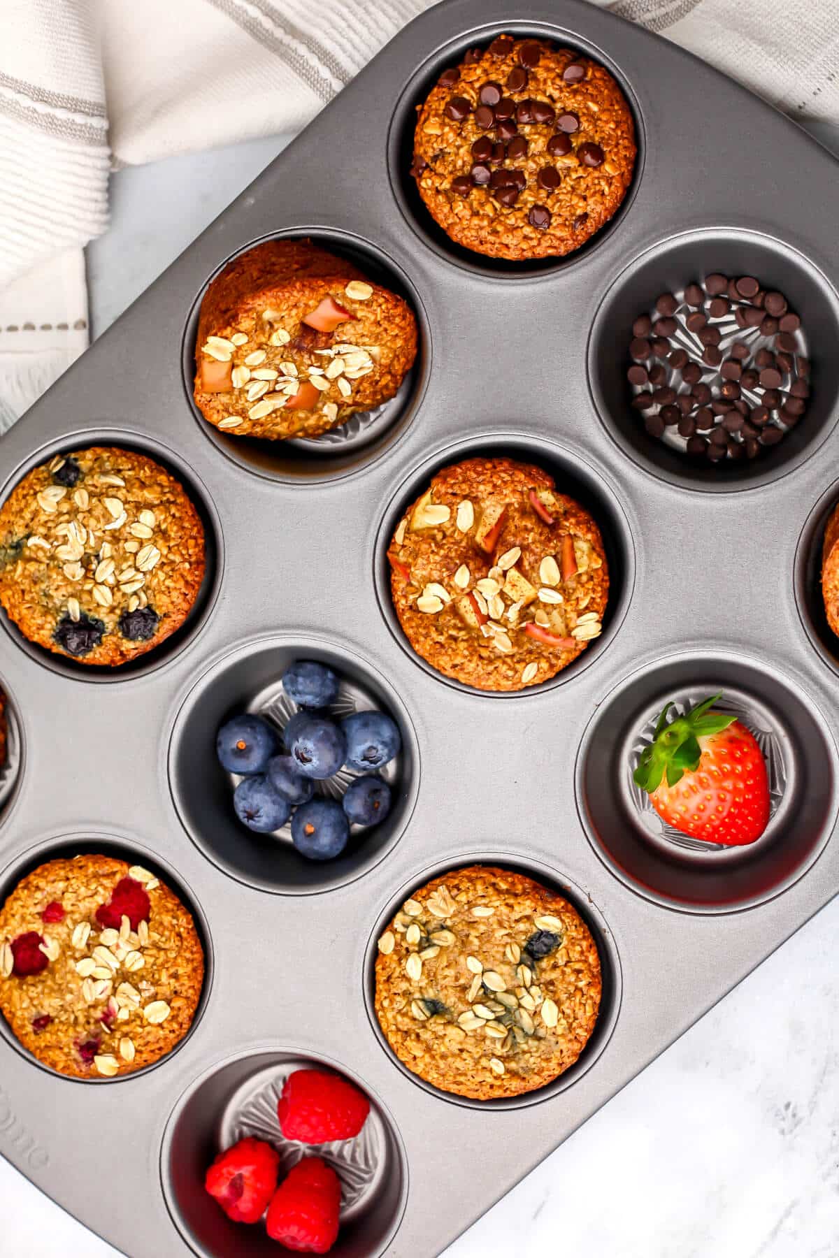 A top view of blender oatmeal cups in many different flavors in a muffin tin with blueberries, raspberries, and strawberries.