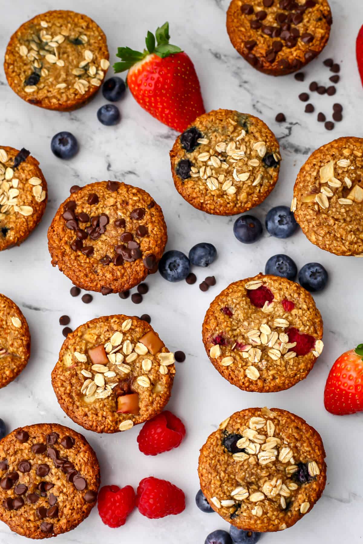 A top view of a variety of flavors of vegan baked oatmeal cups with berries around them.