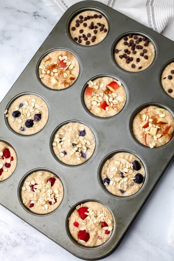 Blender oatmeal poured into a muffin tin with raspberries, blueberries, apples, and chocolate chips in different cups.