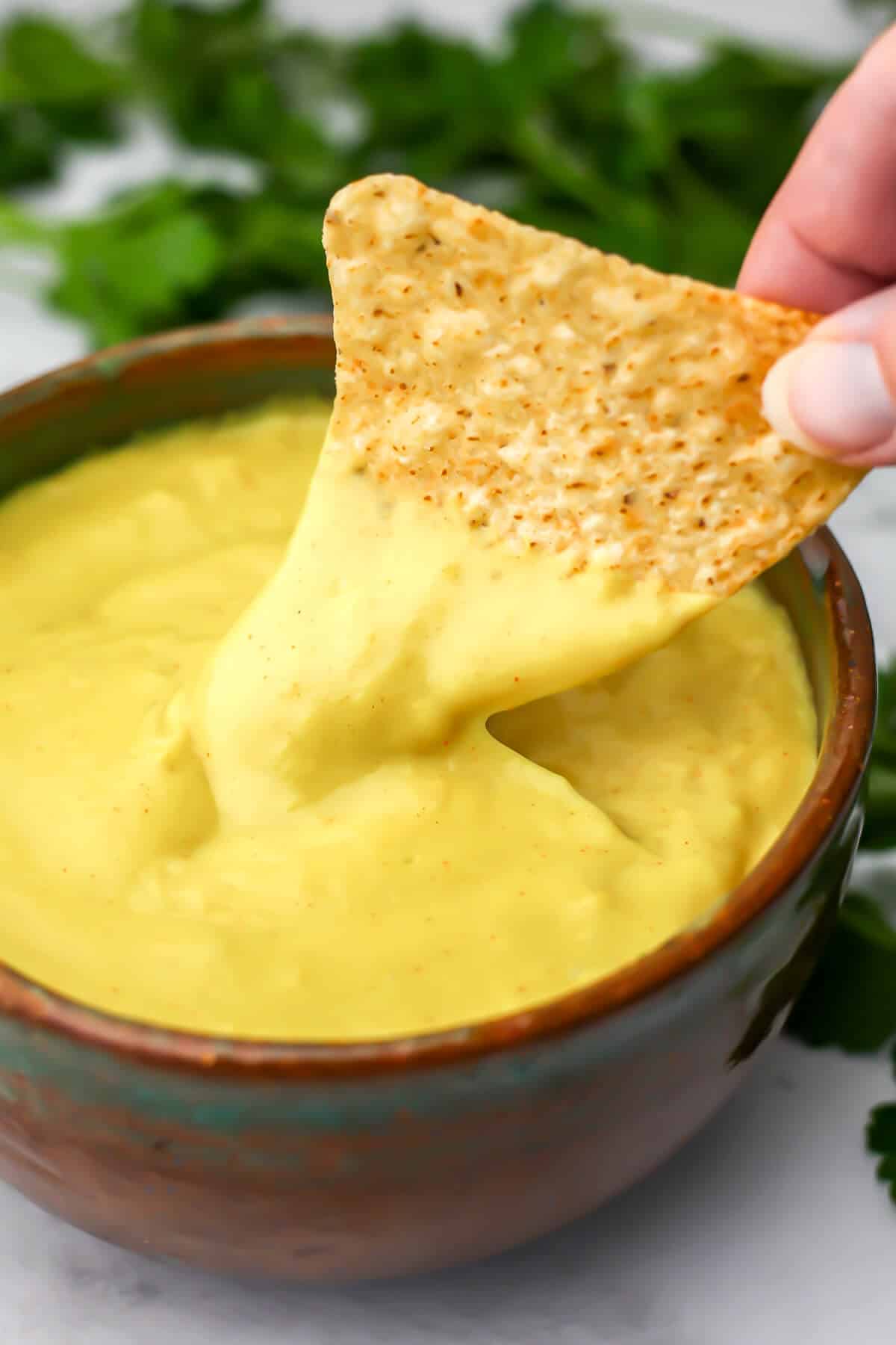 A bowl of vegan cheese sauce with someone dipping a corn chip into it.