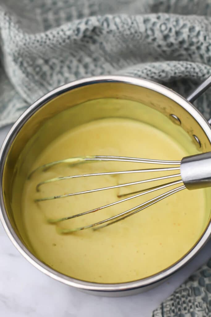 Easy vegan cheese sauce mixed and cooked in a sauce pan being stirred with a whisk.
