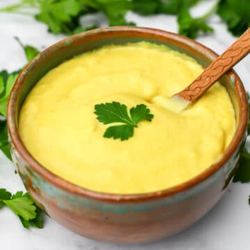 A bowl of vegan cheese sauce with parsley on top and a wooden spoon in it.