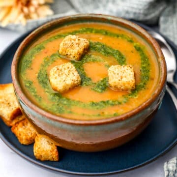 A bowl of creamy vegetable soup with pesto swirled on top and 3 croutons.