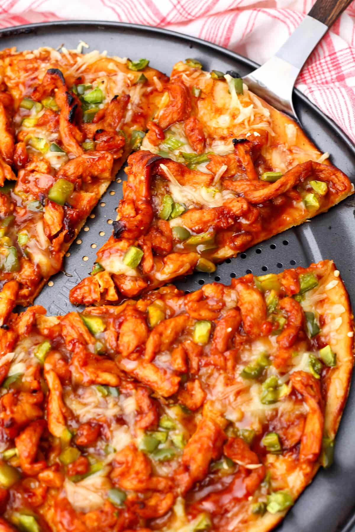 A vegan chicken BBQ pizza made with soy curls and green bell peppers with a slice being taken out of it.