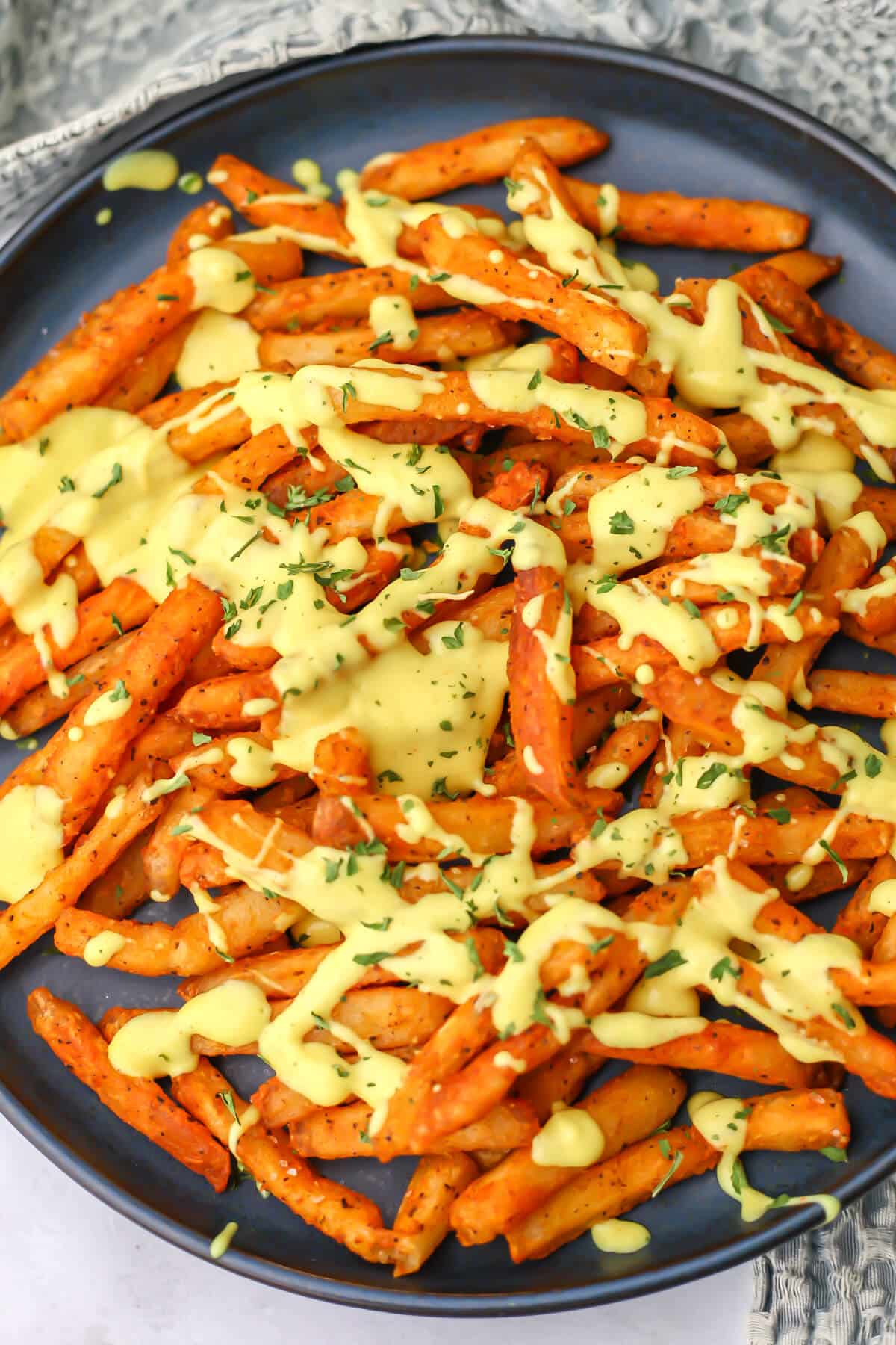 A top view of a plate of French fries drizzled with vegan cheese sauce.
