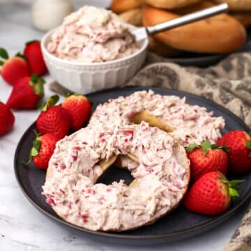 Vegan strawberry cream cheese on a bagel with a bowl of cream cheese behind it.