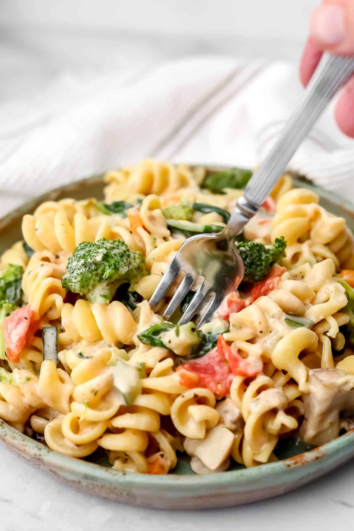A plate full of creamy veggie pasta with a fork sticking into it.