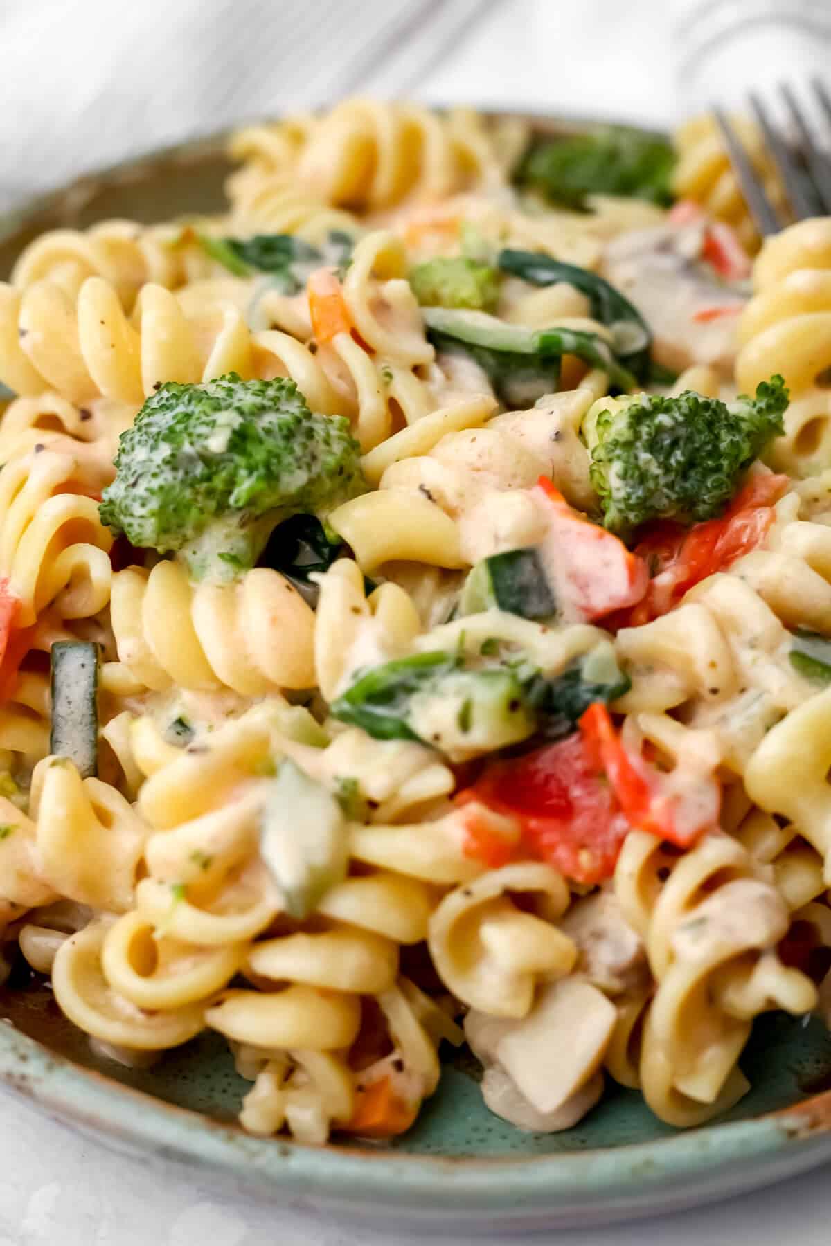 A close up of creamy vegetable pasta on a green plate.