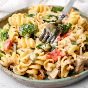 Creamy veggie pasta on a green plate with a fork sticking in it.