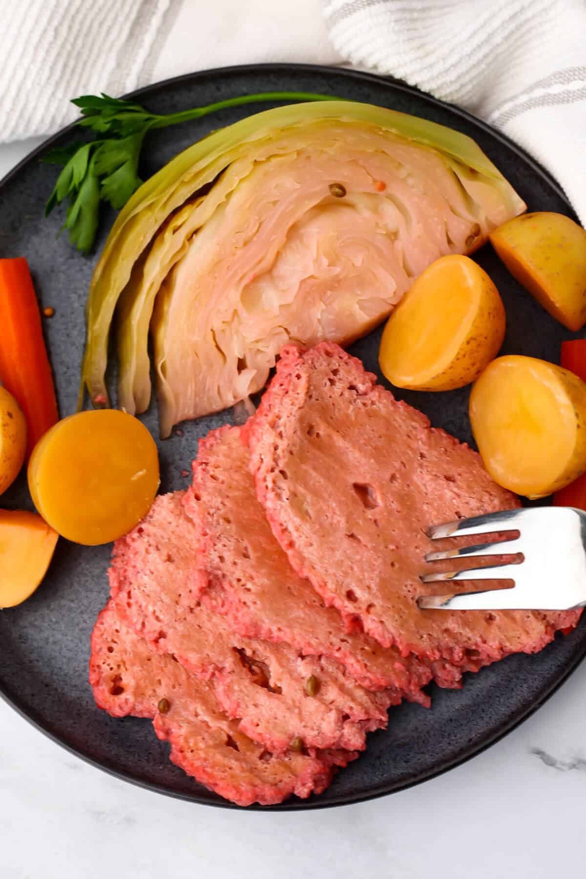 A blue plate with slices of corned beef flavored seitan served with potatoes, carrots, and cabbage.