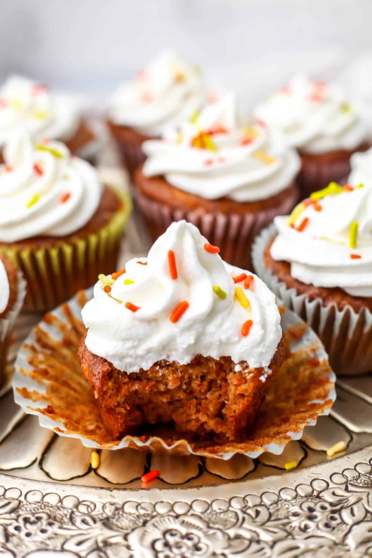 Vegan carrot cake cupcakes with vegan cream cheese frosting with a bite taken out of one of them.