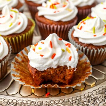 Vegan carrot cake cupcakes on a metal plate with a bite taken out of one of them.
