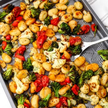 A sheet pan with roasted gnocchi, broccoli, cauliflower, and cherry tomatoes with Italian herbs on it.