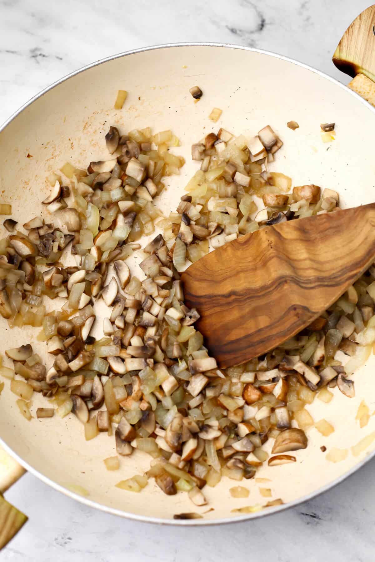 Sauted onions and mushrooms in a white skillet to make vegan quiche.