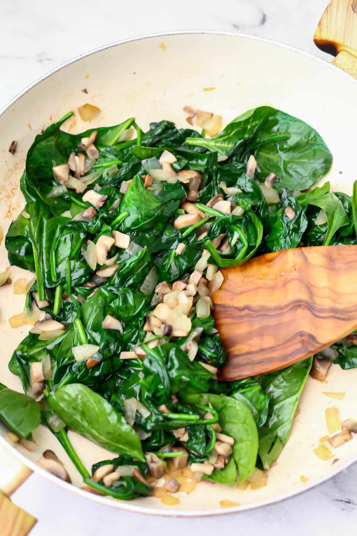 Baby spinach added to onions and mushrooms to make vegan quiche.