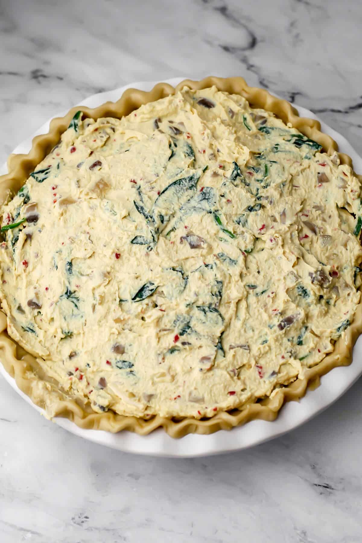 A pie crust with fluted edges filled with a tofu and spinach filling to make vegan quiche.