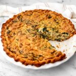 A vegan quiche Lorraine with a piece taken out of it.