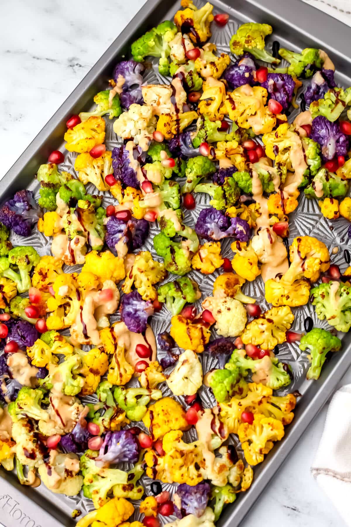 A sheet pan filled with roasted rainbow cauliflower drizzled with tahini, balsamic glaze and pomegranate seeds.