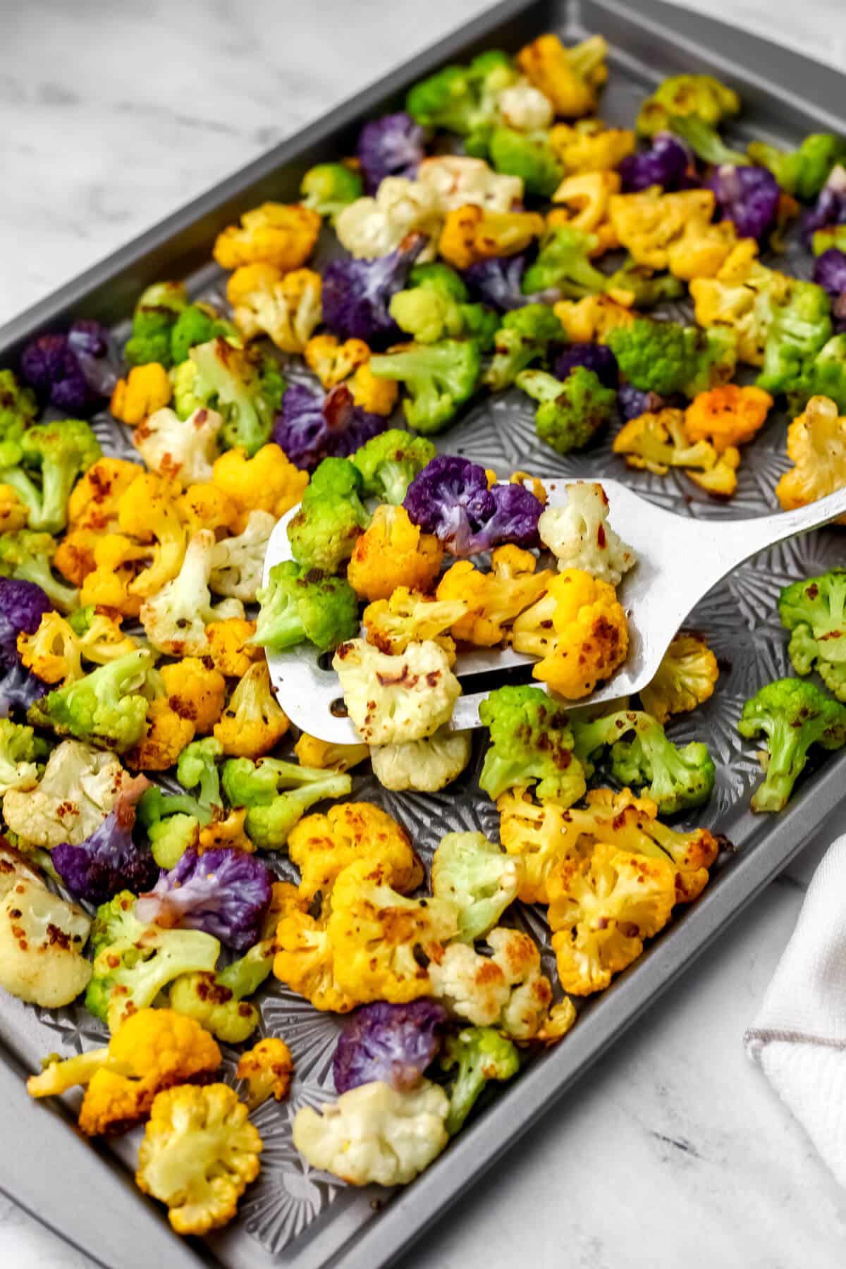 Rainbow cauliflower roasted on a sheet pan being scooped up with a spatula.