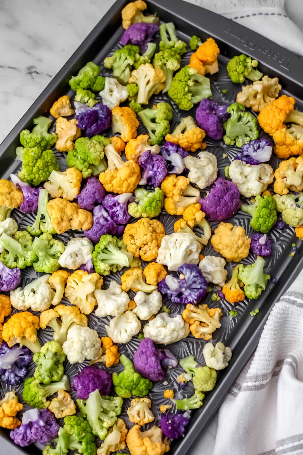 Rainbow cauliflower on a sheet pan coated in olive oil, salt, and pepper before baking.