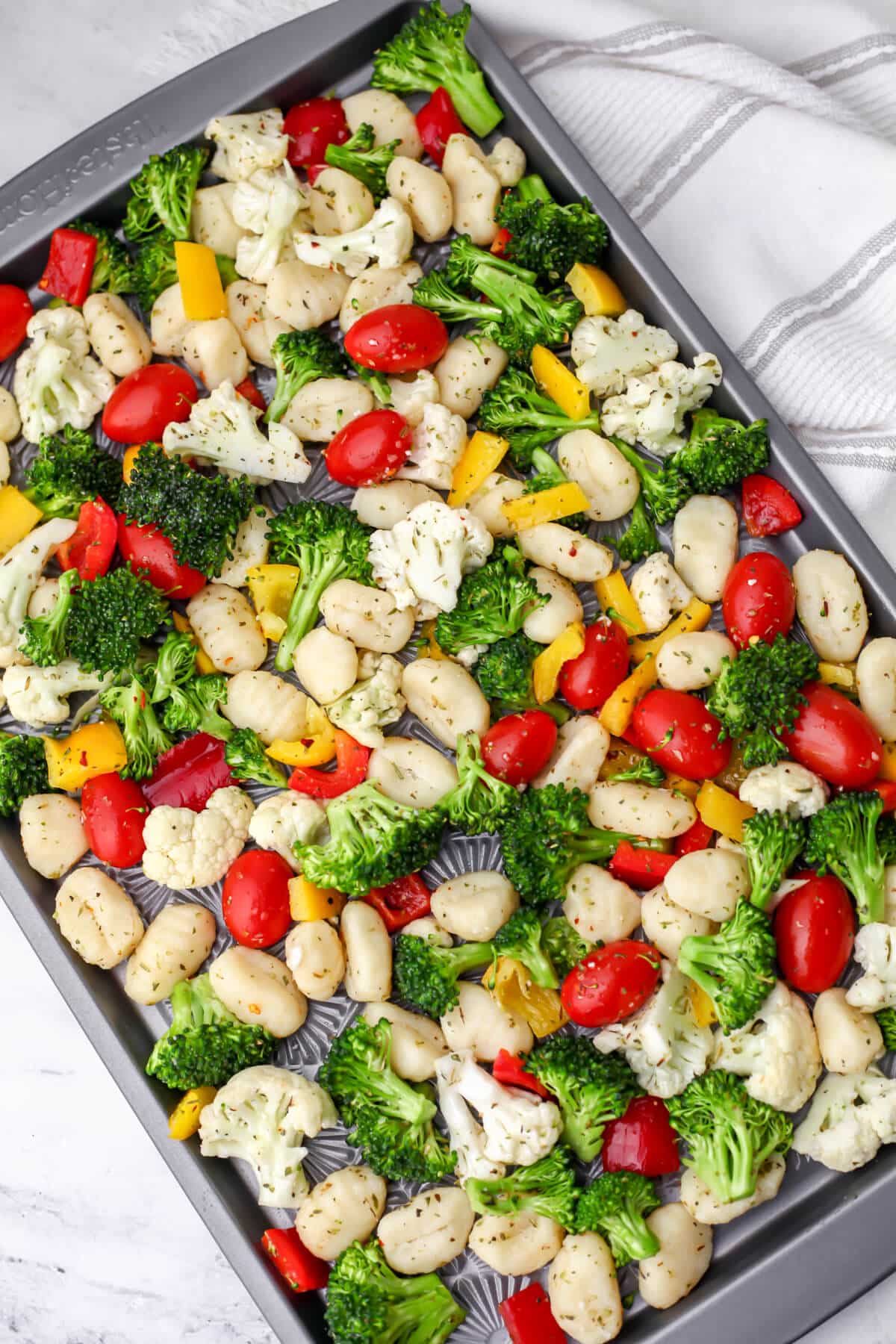A sheet pan filled with gnocchi, broccoli, cauliflower, and bell peppers before baking.
