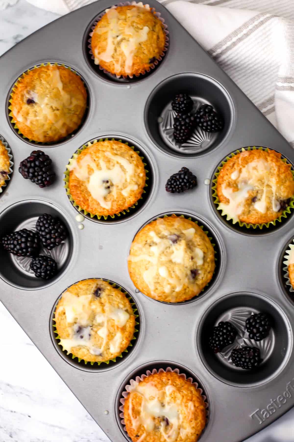 A top view of vegan blackberry muffins in a muffin tin with fresh blackberries filling up some of the muffin cups.