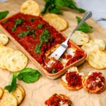 Vegan sun-dried tomato dip in a shallow bowl with some spread on crackers.