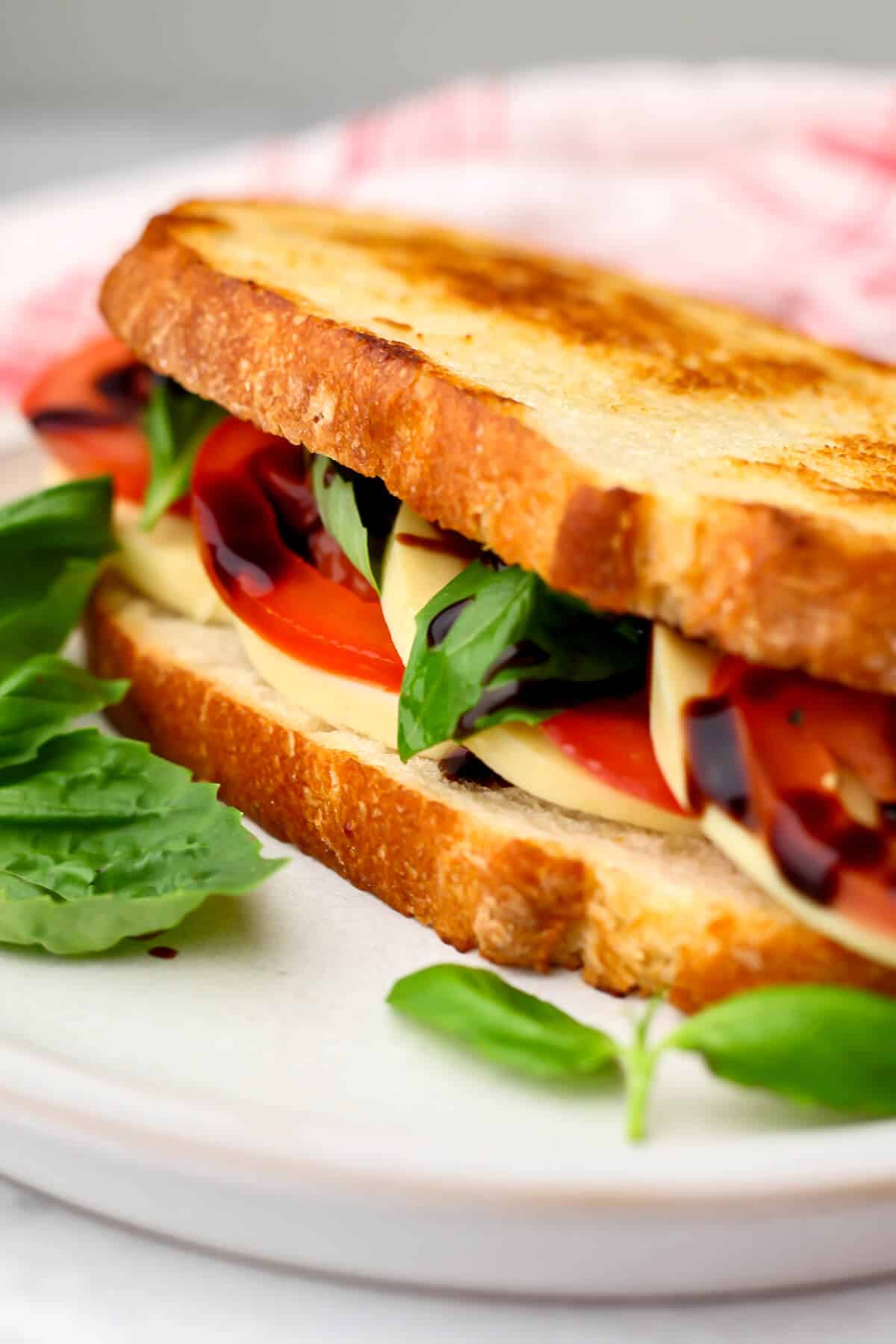 A close up of a vegan Caprese sandwich that has been grilled with a red and white tea towel behind it.