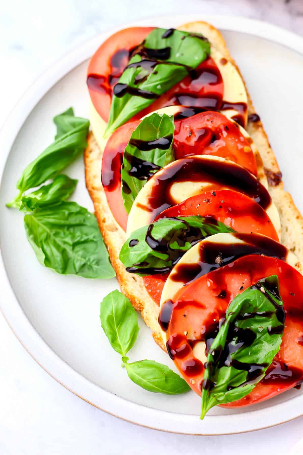 An open face vegan Caprese sandwich with tomatoes, basil, and balsamic glaze.