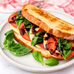 A vegan Caprese sandwich with sliced vegan Mozzarella, fresh tomatoes, and basil,