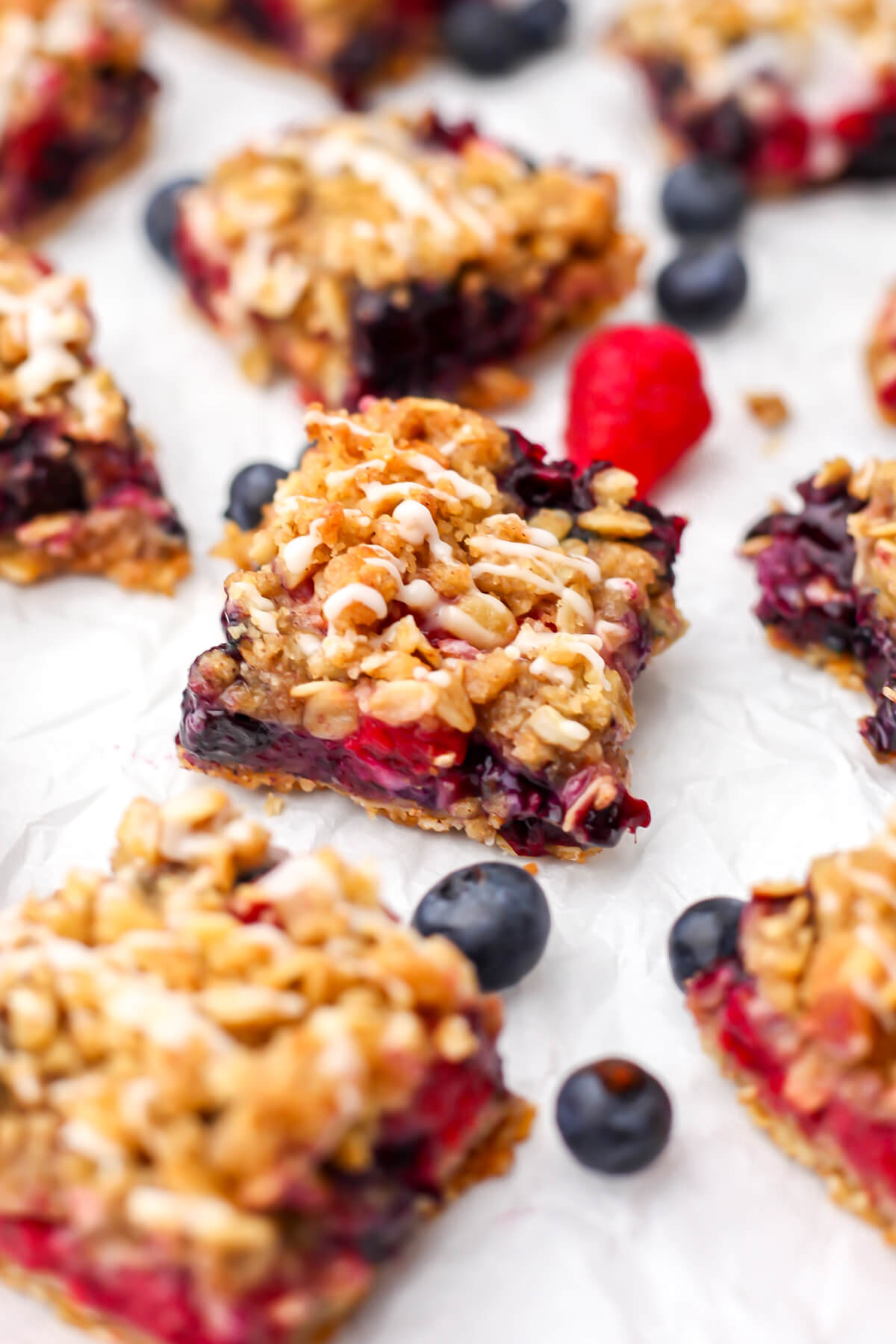 Vegan blueberry and raspberry crumble bars on a piece of white parchment paper with berries around it.