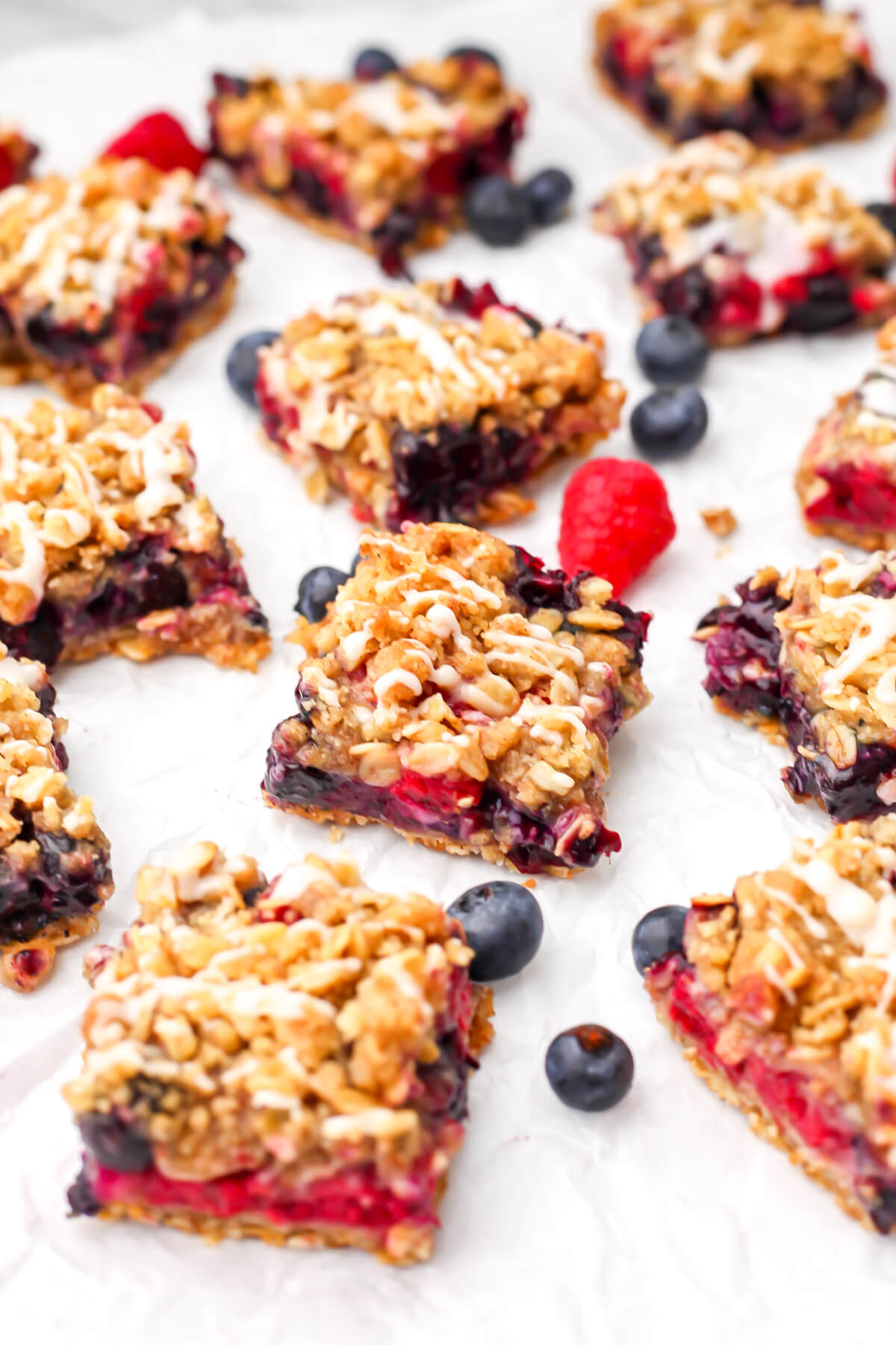 Vegan berry crumble bars with lemon glaze cut into squares on parchment paper.