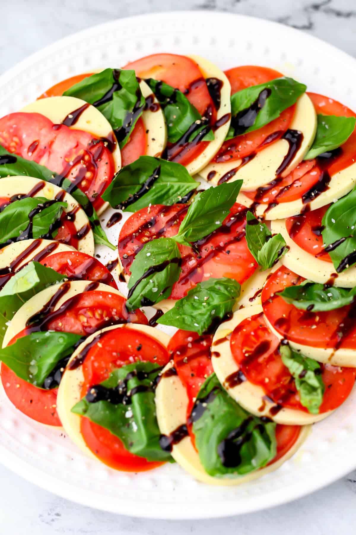 A vegan Caprese salad drizzled with balsamic glaze and olive oil then sprinkled with salt and pepper.