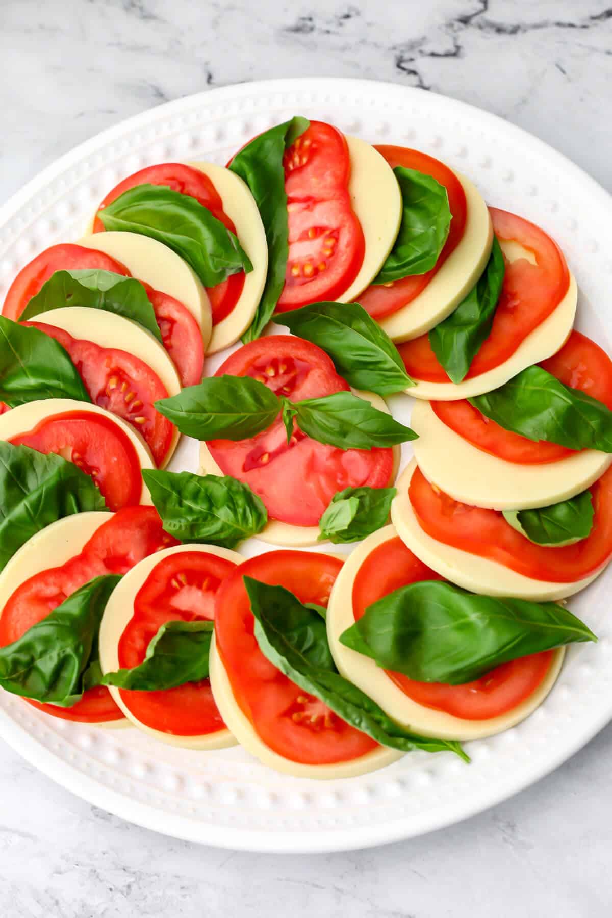 Slices of vegan mozzarella cheese alternating with tomato slices and basil to make a vegan Caprese salad.
